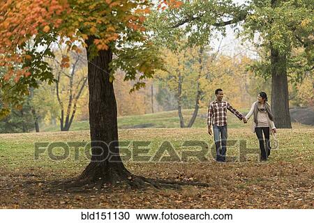 Stock Image - Couple holding hands and walking in park. Fotosearch