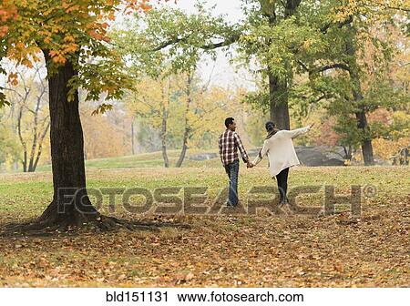 Stock Image - Couple holding hands and walking in park. Fotosearch