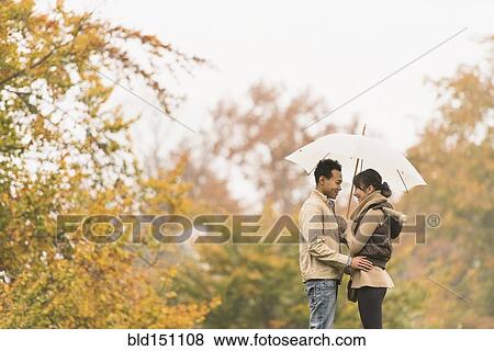 Stock Photo - Couple standing with umbrella in park. Fotosearch