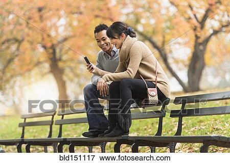Couple using cell phone on park bench View Large Photo Image Stock Photo - Couple using cell phone on park bench. Fotosearch
