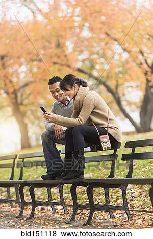 Stock Photo - Couple using cell phone on park bench. Fotosearch