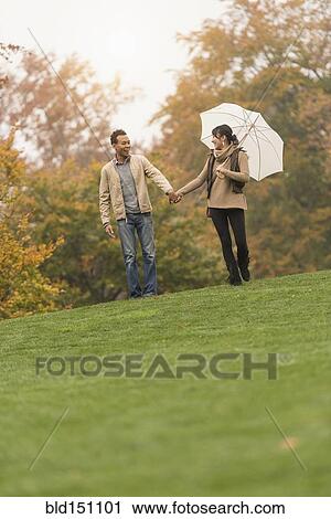 Couple walking with umbrella in park View Large Photo Image Stock Image - Couple walking with umbrella in park. Fotosearch