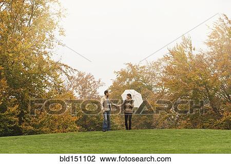 Stock Image - Couple walking with umbrella in park. Fotosearch