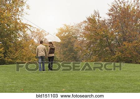 Stock Image - Couple walking with umbrella in park. Fotosearch