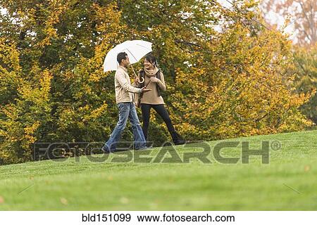 Couple walking with umbrella in park View Large Photo Image Stock Photo - Couple walking with umbrella in park. Fotosearch