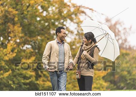 Couple walking with umbrella in park View Large Photo Image Stock Photo - Couple walking with umbrella in park. Fotosearch
