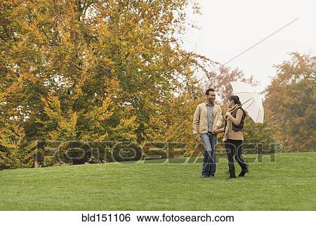 Stock Photograph - Couple walking with umbrella in park. Fotosearch