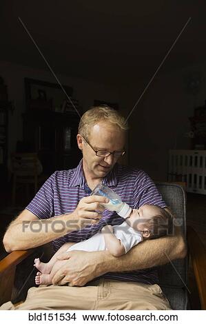 Father bottle feeding baby in armchair View Large Photo Image Picture - Father bottle feeding baby in armchair. Fotosearch