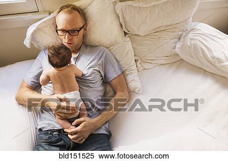 Stock Photography - Father playing with baby on bed. Fotosearch