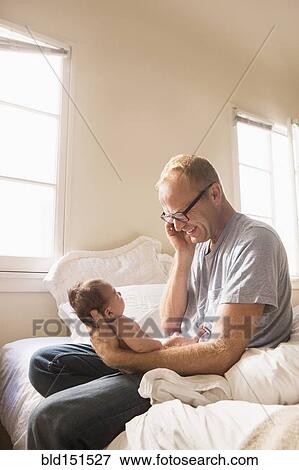Father talking on cell phone and holding baby on bed View Large Photo Image Stock Photo - Father talking on cell phone and holding baby on bed. Fotosearch