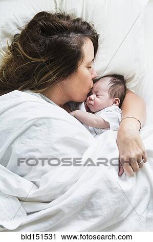 Stock Image - High angle view of mother kissing baby in bed. Fotosearch