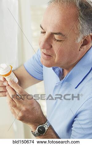 Picture - Hispanic man reading prescription medication bottle. Fotosearch