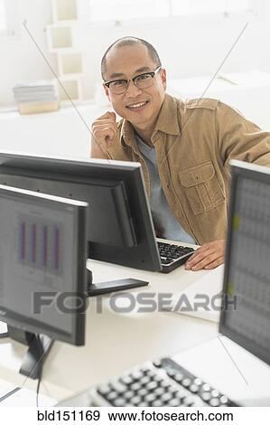 Korean businessman smiling at computer at office desk View Large Photo Image Stock Photo - Korean businessman smiling at computer at office desk. Fotosearch