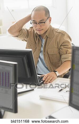 Stock Photo - Korean businessman working on computer at office desk. Fotosearch