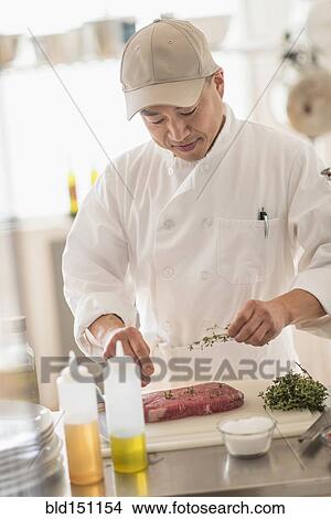 Picture - Korean chef seasoning meat in kitchen. Fotosearch