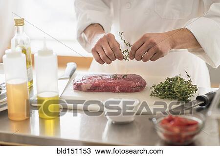 Stock Image - Korean chef seasoning meat in kitchen. Fotosearch