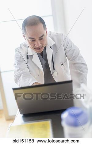 Stock Photo - Korean doctor using laptop in office. Fotosearch