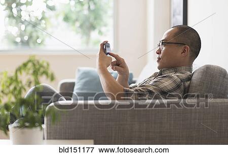 Stock Photo - Korean man using cell phone on sofa. Fotosearch