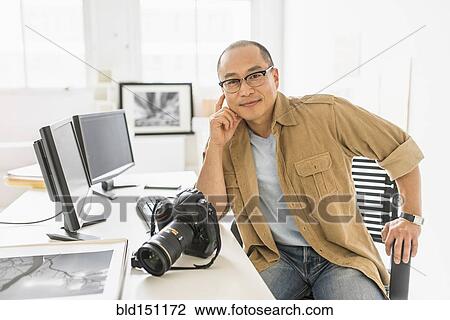 Stock Image - Korean photographer smiling at desk. Fotosearch