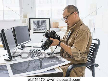 Stock Image - Korean photographer using camera at desk. Fotosearch
