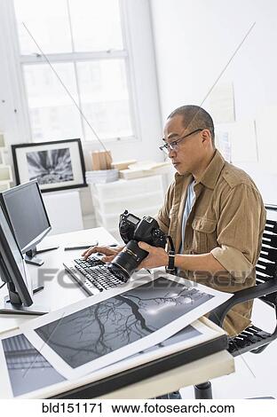 Stock Image - Korean photographer using computer at desk. Fotosearch