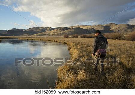 Stock Photo - Man carrying fishing supplies near river. Fotosearch