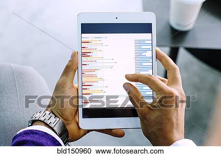 Stock Image - Mixed race businessman examining graph on digital tablet. Fotosearch