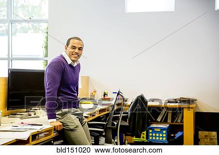 Mixed race businessman smiling at office desk View Large Photo Image Stock Image - Mixed race businessman smiling at office desk. Fotosearch