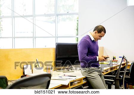 Stock Image - Mixed race businessman using cell phone at office desk. Fotosearch