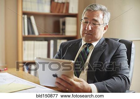 Stock Photo - Mixed race businessman using digital tablet at desk in office. Fotosearch