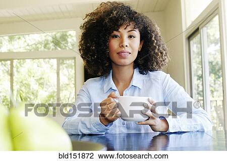 Stock Image - Mixed race businesswoman drinking coffee at table. Fotosearch