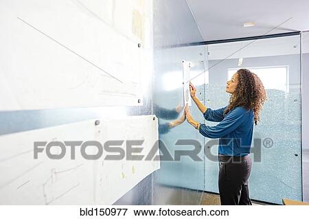 Stock Photo - Mixed race businesswoman hanging paper on magnetic office wall. Fotosearch