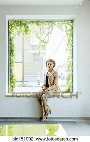 Stock Image - Mixed race businesswoman smiling in office window. Fotosearch