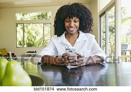 Picture - Mixed race businesswoman using cell phone at table. Fotosearch