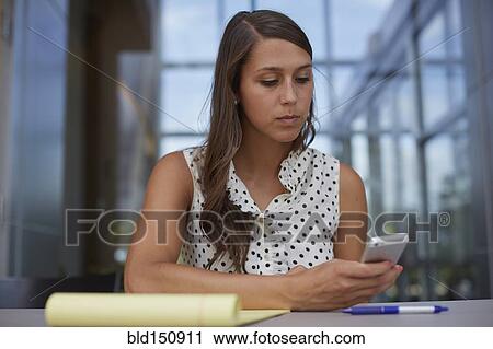 Stock Image - Mixed race businesswoman using cell phone at desk. Fotosearch