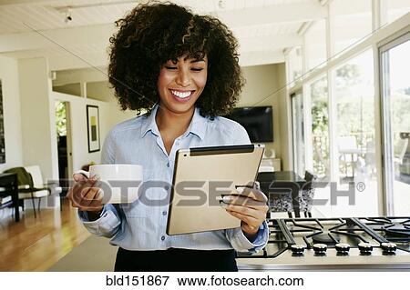 Stock Photo - Mixed race businesswoman using digital tablet in domestic kitchen. Fotosearch