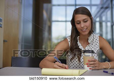 Stock Image - Mixed race businesswoman writing on notepad at desk. Fotosearch