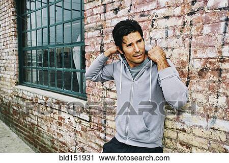 Stock Image - Mixed race man leaning on brick building. Fotosearch