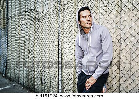 Picture - Mixed race man leaning on chain link fence. Fotosearch