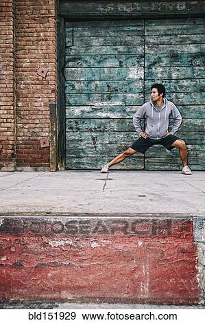 Stock Photo - Mixed race man stretching near industrial building. Fotosearch