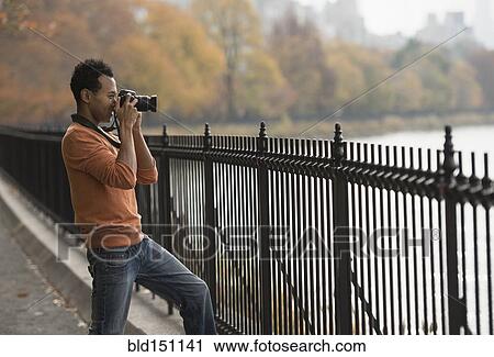 Stock Image - Mixed race man taking photograph on waterfront. Fotosearch