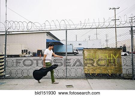 Stock Image - Mixed race musician carrying guitar case on sidewalk. Fotosearch
