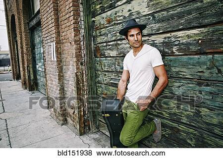 Mixed race musician holding guitar case near industrial building View Large Photo Image Stock Photo - Mixed race musician holding guitar case near industrial building. Fotosearch