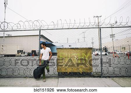 Stock Photograph - Mixed race musician leaning on fence holding guitar case. Fotosearch