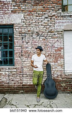 Stock Image - Mixed race musician with guitar case using cell phone. Fotosearch