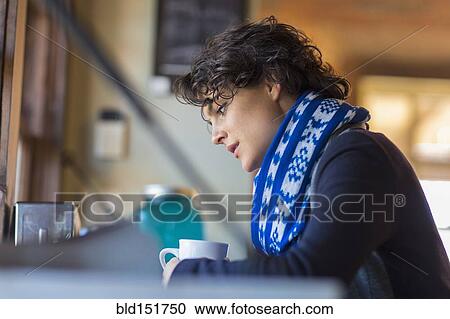 Stock Image - Mixed race woman drinking cup of coffee in cafe. Fotosearch