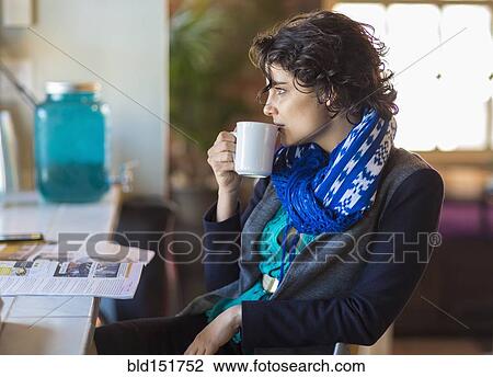 Stock Image - Mixed race woman drinking cup of coffee in cafe. Fotosearch