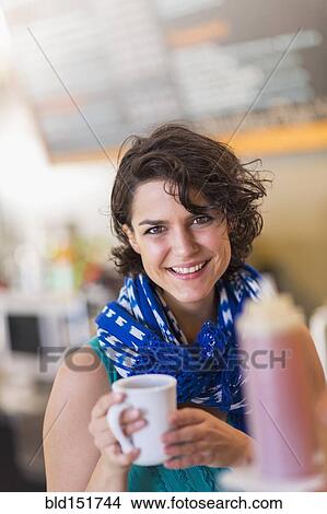 Picture - Mixed race woman holding cup of coffee in cafe. Fotosearch