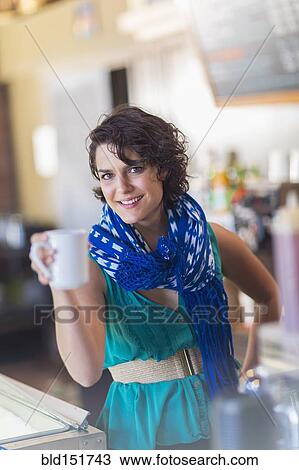 Stock Image - Mixed race woman holding cup of coffee in cafe. Fotosearch