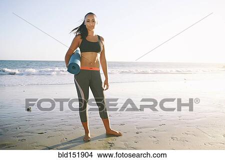 Picture - Mixed race woman holding yoga mat on beach. Fotosearch